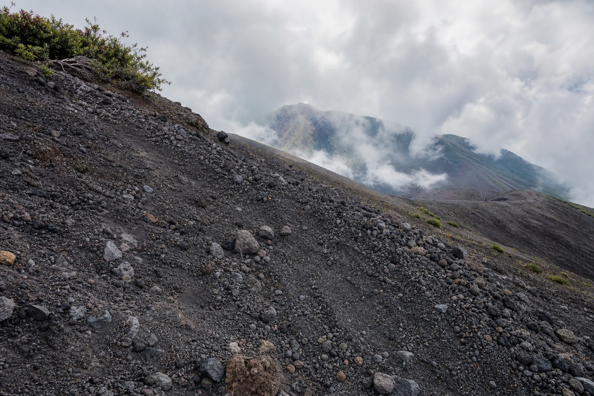 Loose grey volcanic rock on the upper trail near the summit of Santa Ana volcano with cloud drifting across the slope