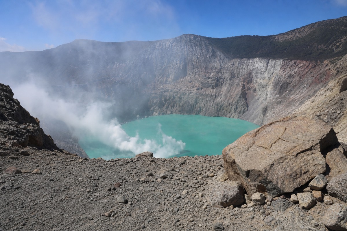 Bare volcanic rock at the managed edge of the Santa Ana crater rim with sulfur steam rising from the lake below