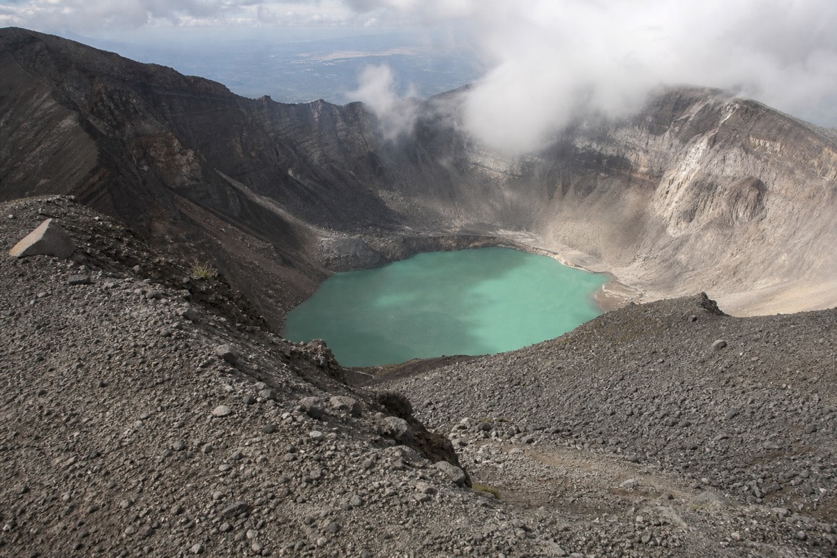 Windswept crater rim of Santa Ana volcano with the turquoise lake below and cloud streaming past the far wall