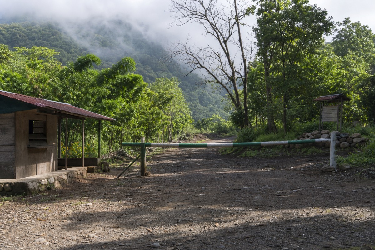 Simple wooden fee booth at the volcano trailhead in the morning with a hand-painted barrier and cloud forest behind