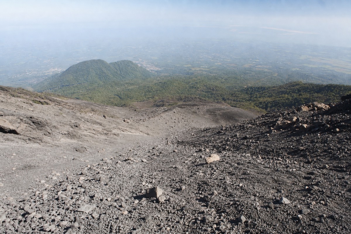 Looking down the loose grey volcanic rock of the upper Santa Ana trail toward forested slopes far below