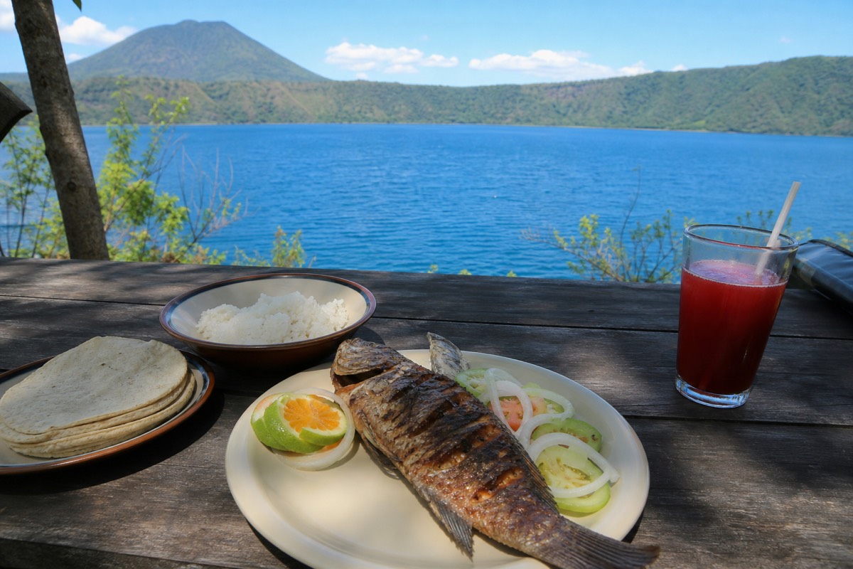 Lakeside lunch table with a plate of grilled food overlooking the deep blue water of Lake Coatepeque with volcano slopes beyond