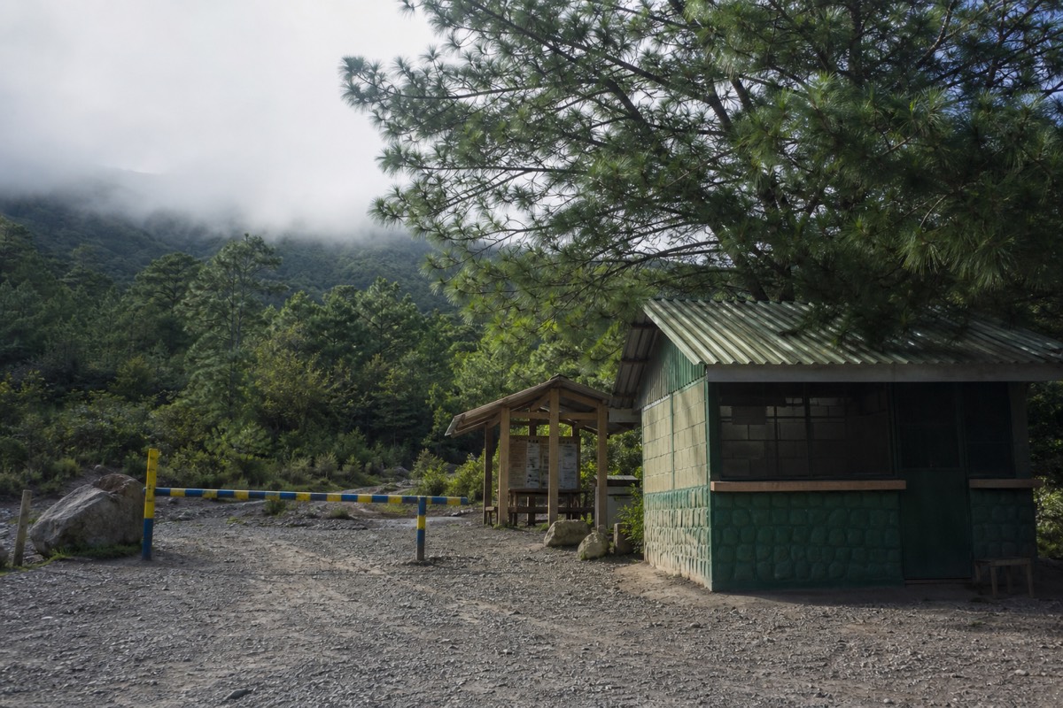 Simple ranger post and painted barrier at a highland volcano trailhead in El Salvador with mist behind the pines