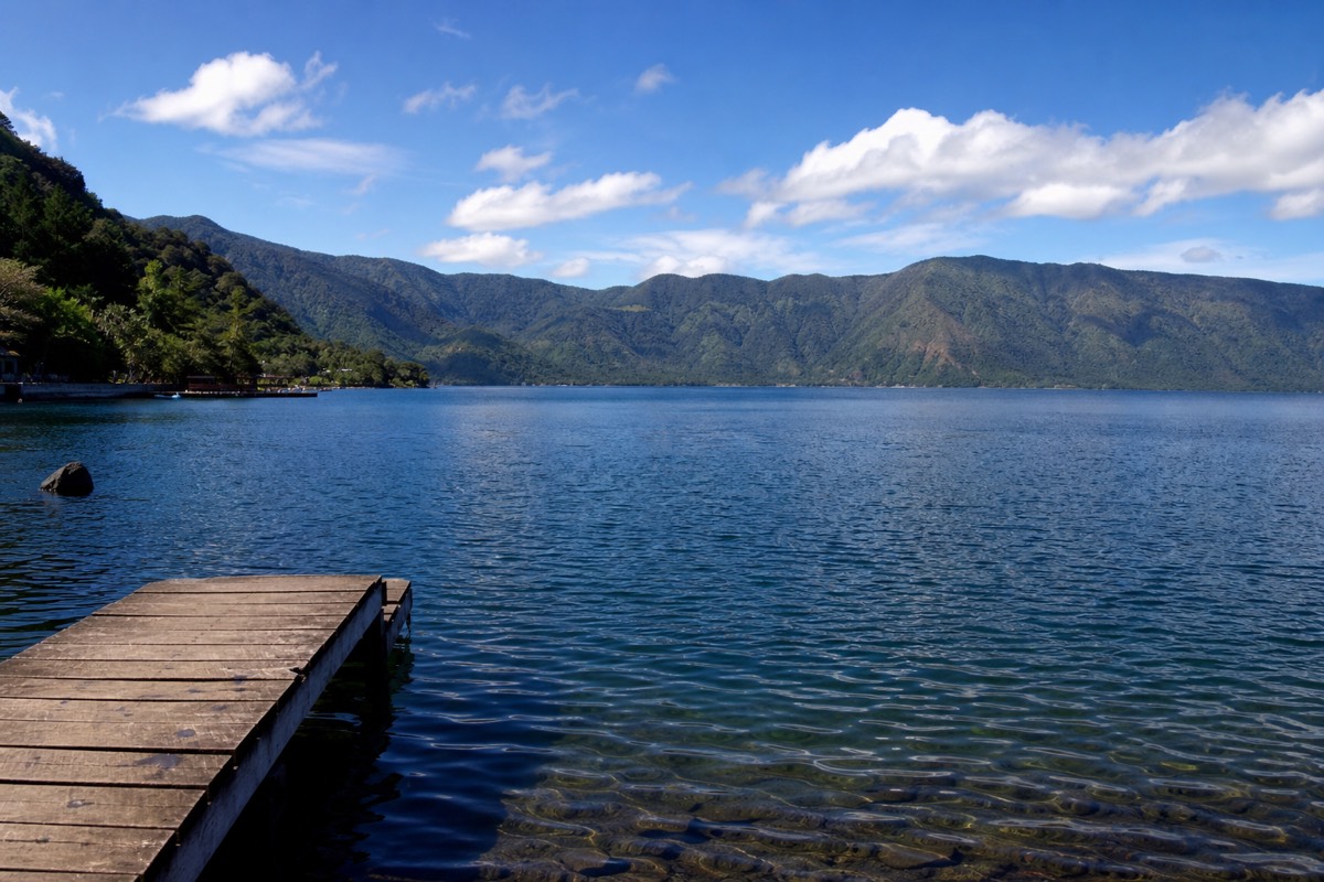 Calm blue water of Lake Coatepeque with wooden lakeside decks and green caldera walls behind