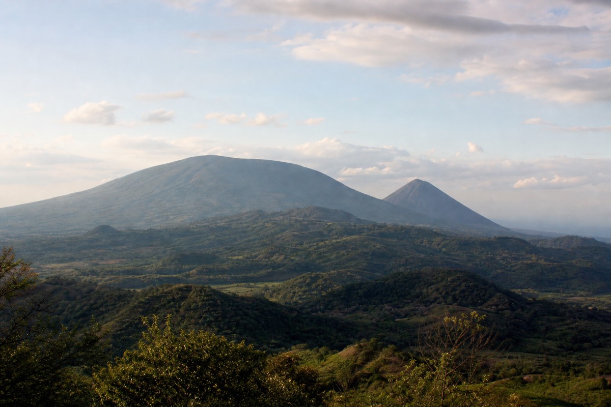 Santa Ana Volcano's broad forested summit and Izalco's dark cone together on the skyline above green ridges in soft afternoon light