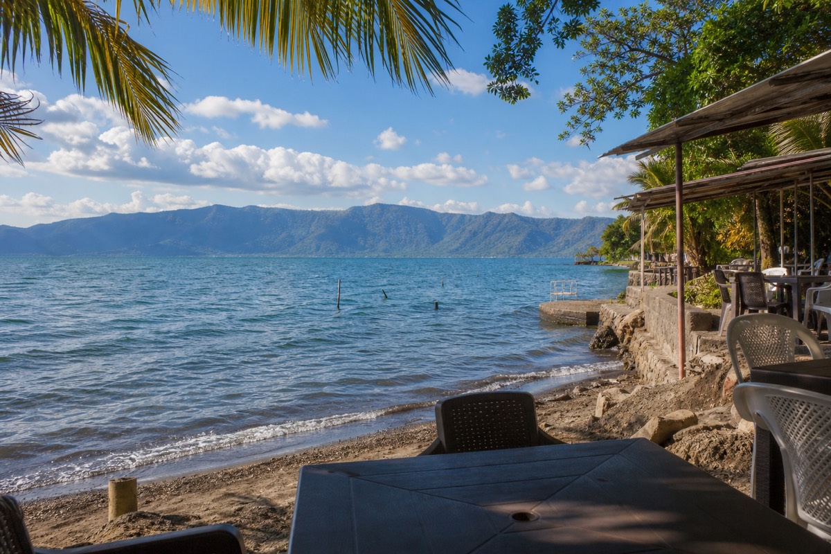 Afternoon light on the shore of Lake Coatepeque with lakeside restaurant terraces, palm shade and the wide blue caldera beyond