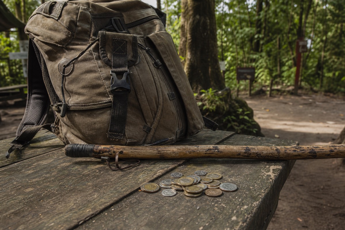 Small pile of US coins beside a worn daypack and a rented wooden walking pole on a bench at the forest trailhead of Santa Ana Volcano