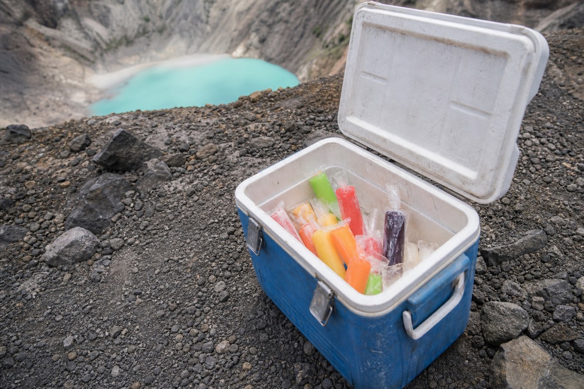 Insulated cooler of fruit paletas open on the rocky crater rim of Santa Ana Volcano with the turquoise crater lake blurred far below