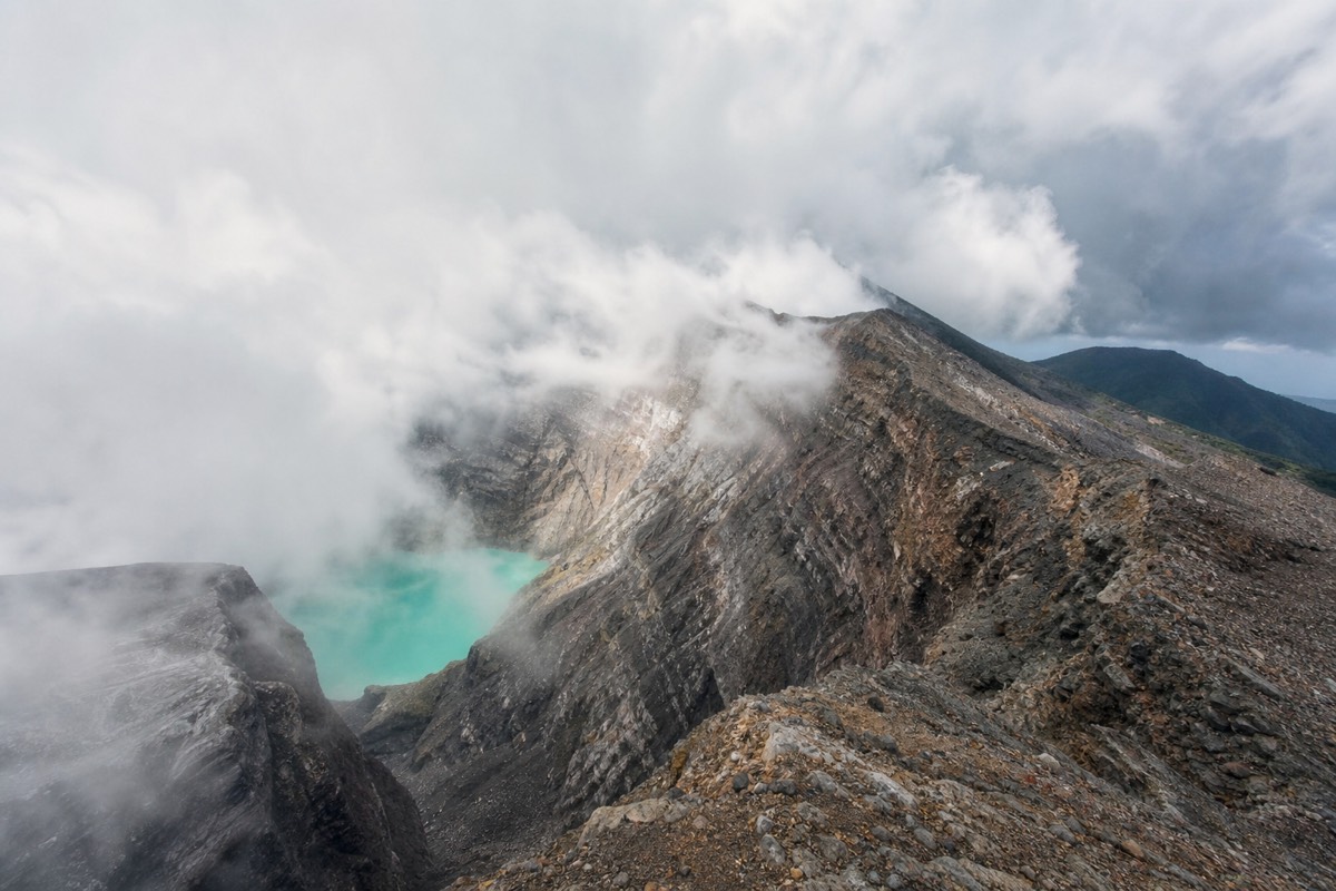 Wisps of cloud sweeping across the rocky crater rim of Santa Ana Volcano with a patch of turquoise crater lake showing through the gap