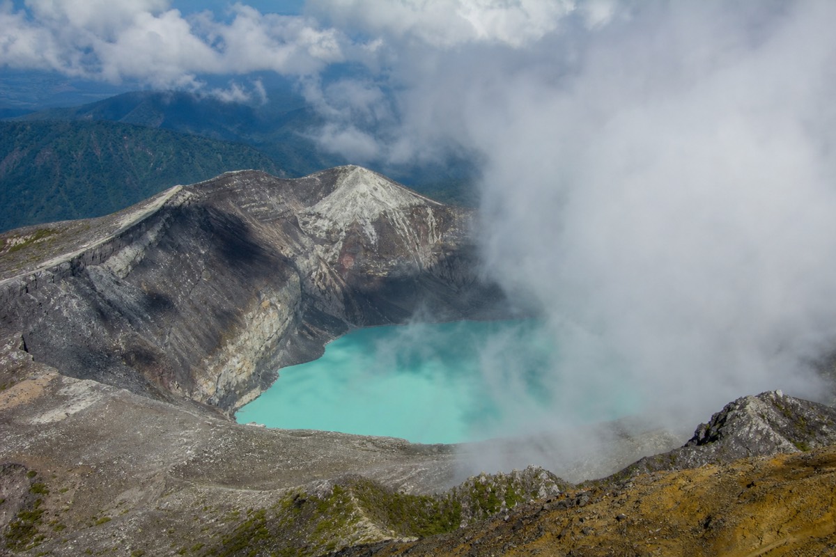 Wind-driven cloud tearing open above the crater lake of Santa Ana Volcano with grey rock walls and turquoise water partly revealed