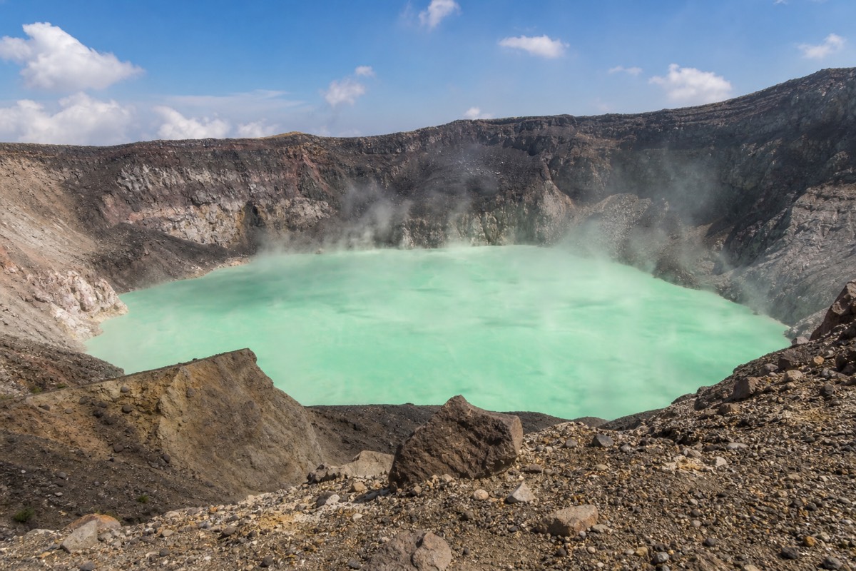 Wisps of steam rising off the turquoise acidic crater lake of Santa Ana volcano seen from the bare rock of the rim