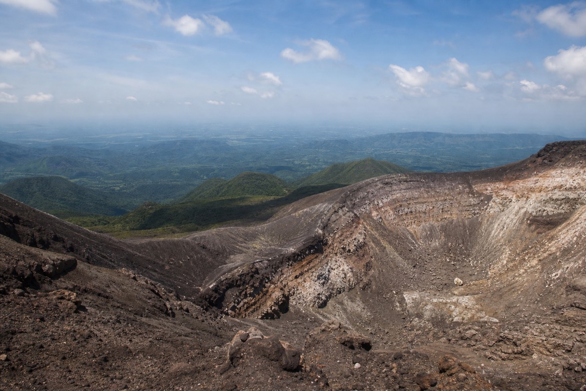 Wide view from the Santa Ana volcano summit rim across the crater and out to distant green ridges and haze