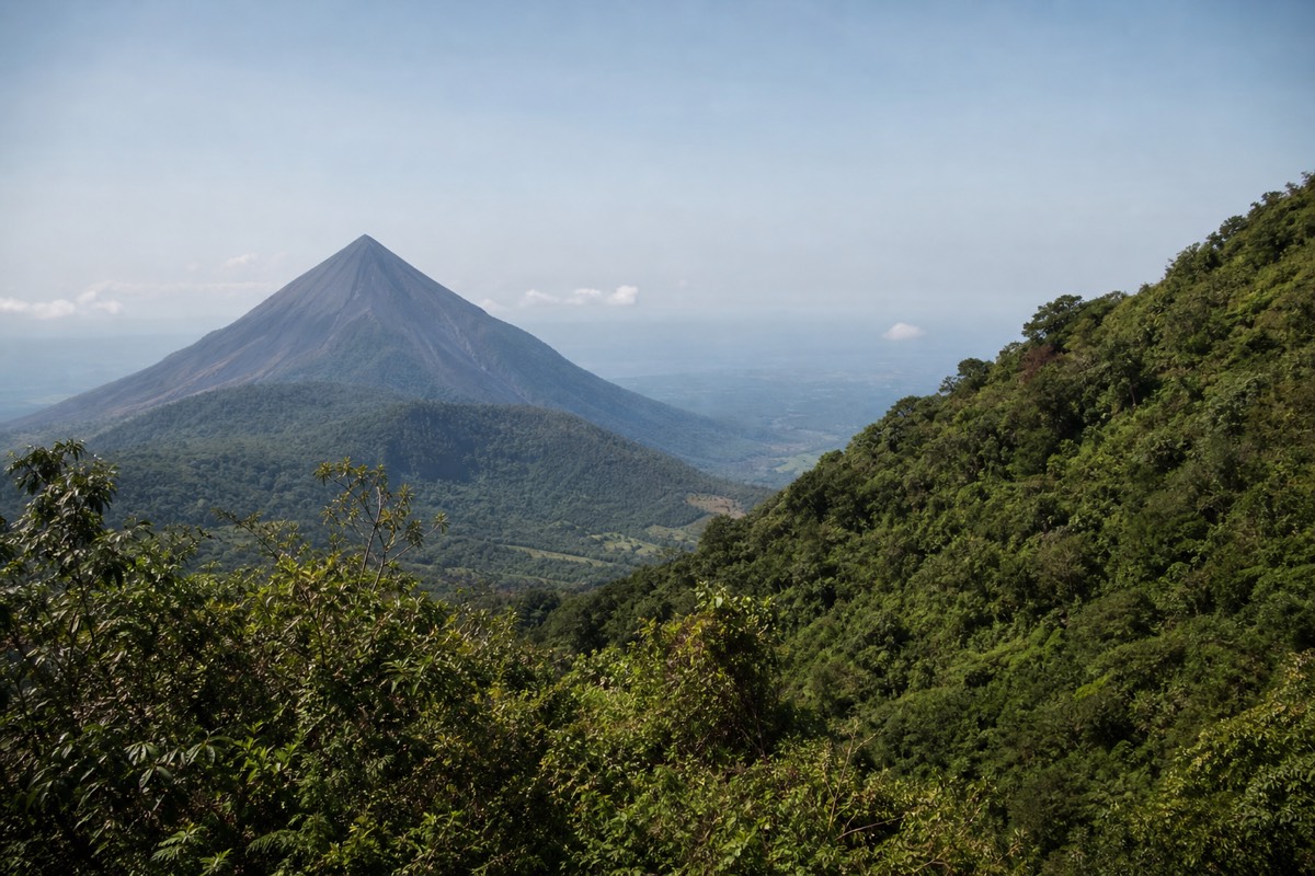 The bare black cone of Izalco volcano seen across the valley from the Santa Ana volcano trail, sharp against hazy sky