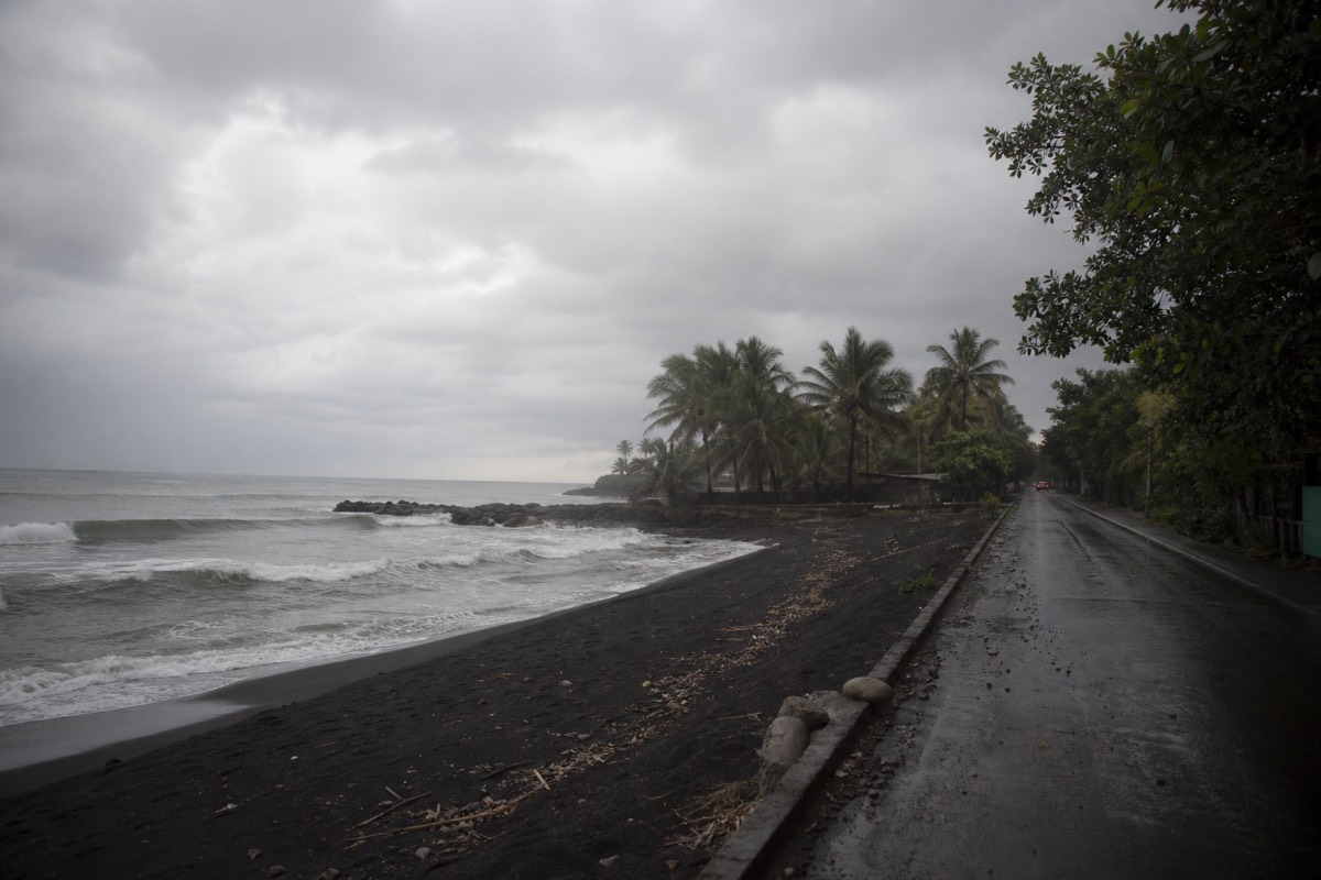 Grey dawn over a black sand surf beach in El Salvador with a wet road leading inland from the palms