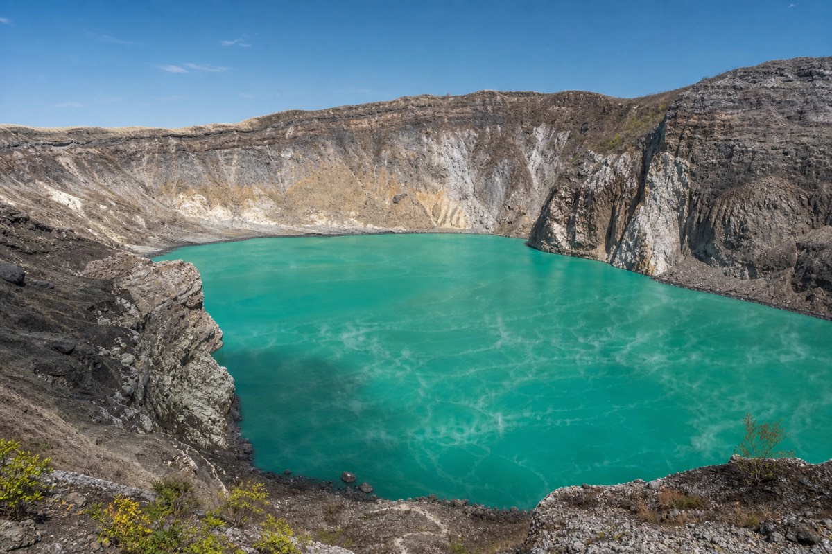 Vivid turquoise acid lake filling a steep-walled volcanic crater in El Salvador under a clear dry-season sky