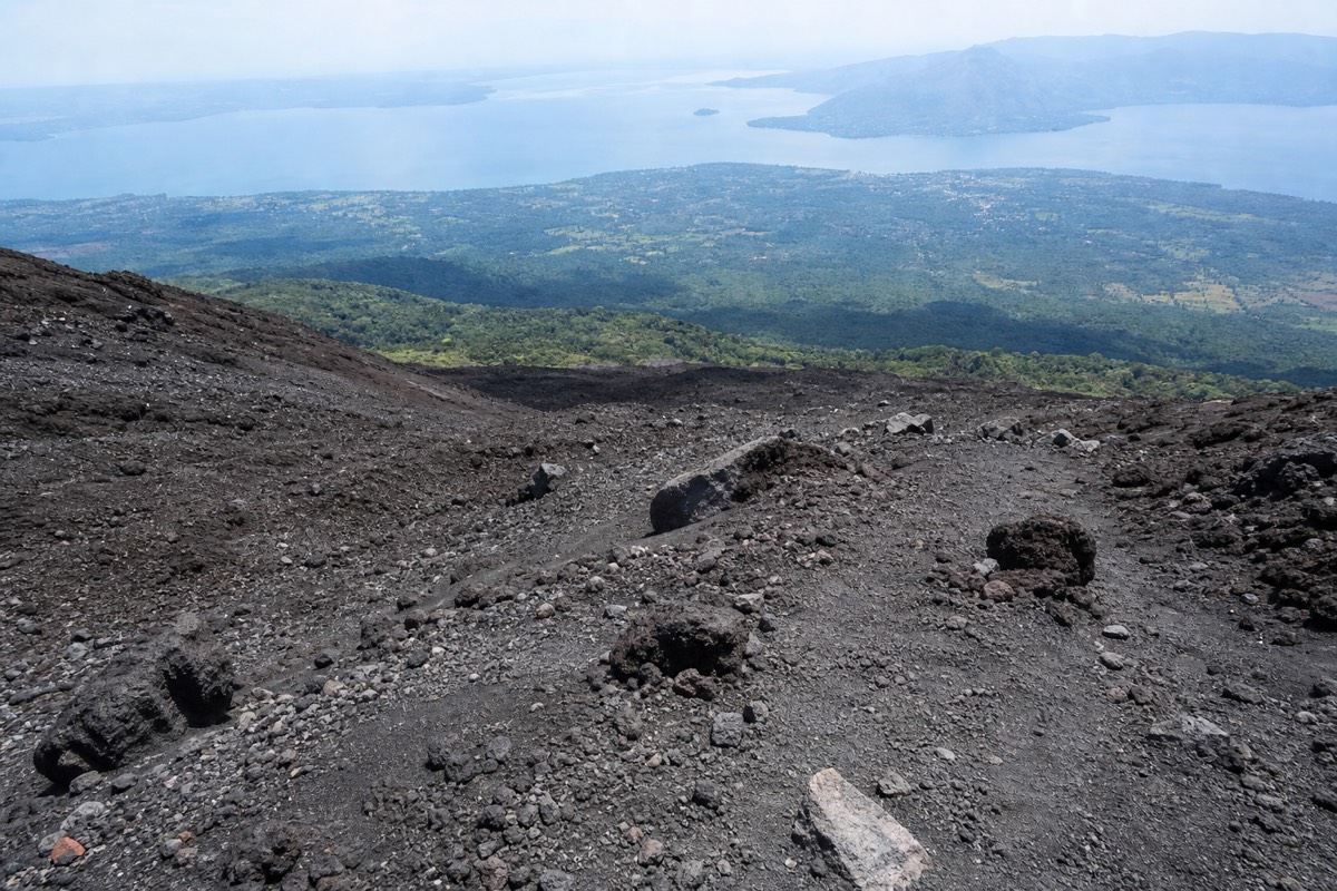 Loose grey volcanic gravel on the upper Santa Ana trail seen looking downhill toward green lowlands and Lake Coatepeque in haze