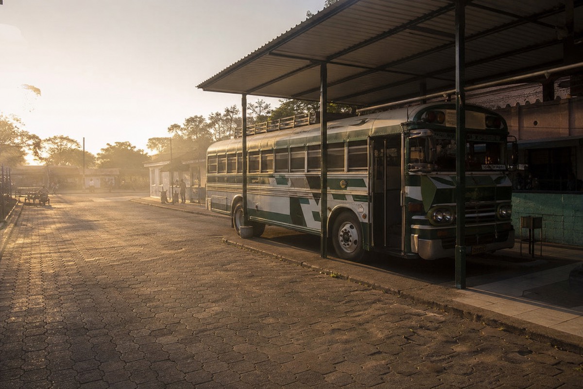 Early morning at a bus terminal in Santa Ana city, El Salvador, with a local bus waiting under warm light