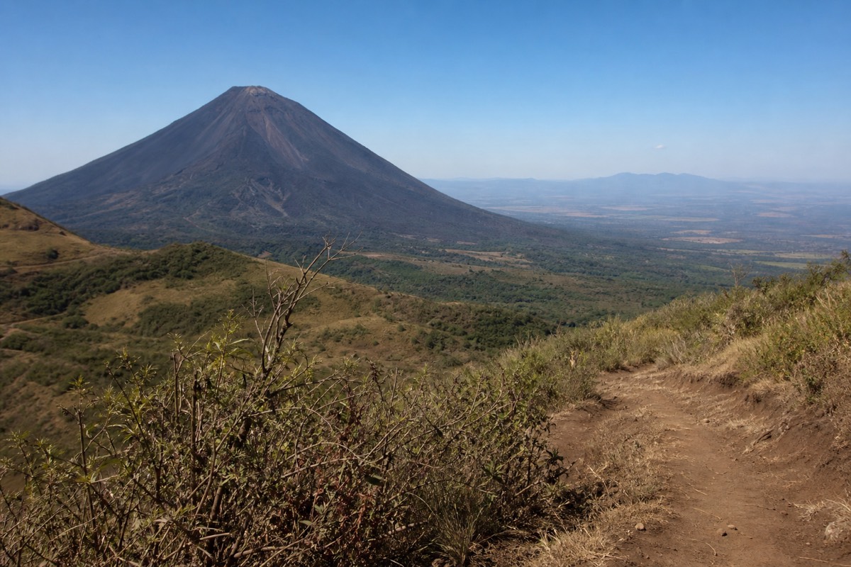 Open middle slopes of the Santa Ana volcano trail with the dark cone of Izalco across the valley under a clear sky