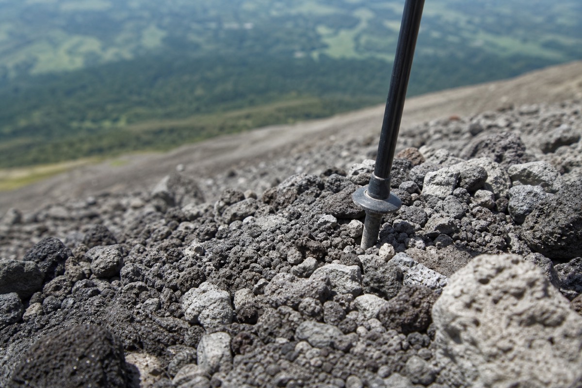 Close view of the loose volcanic rock and gravel on the upper Santa Ana volcano trail with a trekking pole tip planted between stones