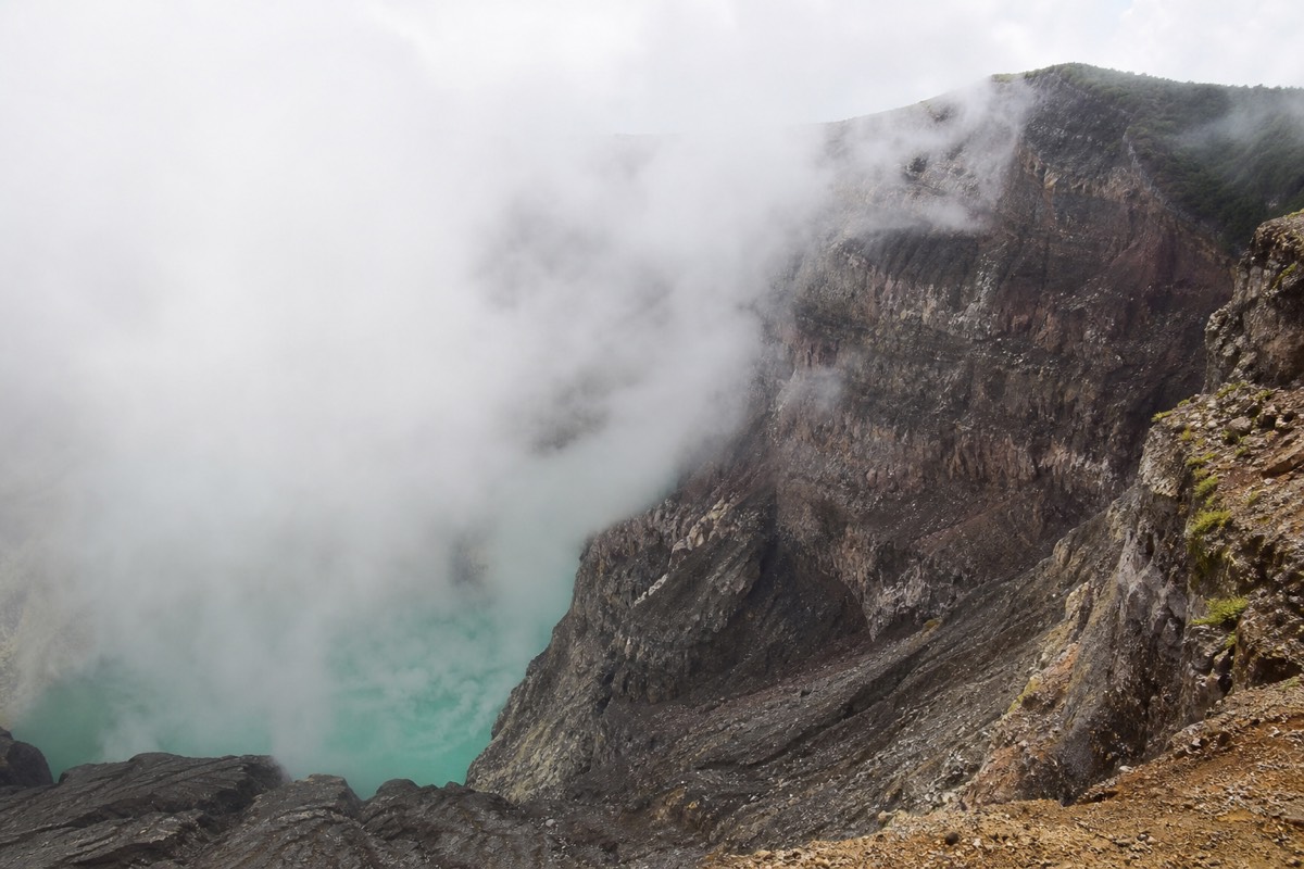 Cloud drifting over the bare rock of the Santa Ana volcano crater rim with turquoise water partly visible below