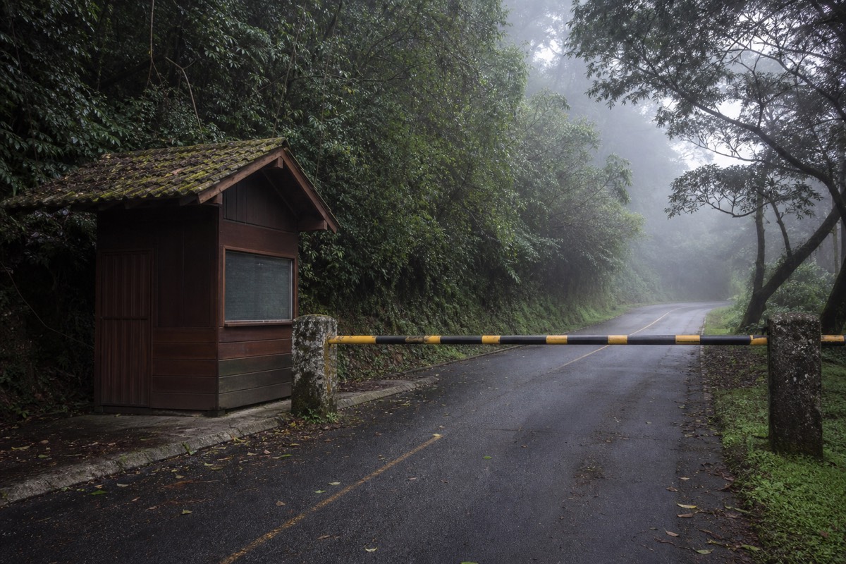 Wooden entrance booth and barrier at the Cerro Verde park gate surrounded by cloud forest, morning mist on the road