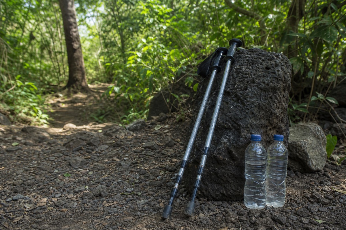 Two rental trekking poles leaning against a rock beside two full water bottles at the volcano trailhead