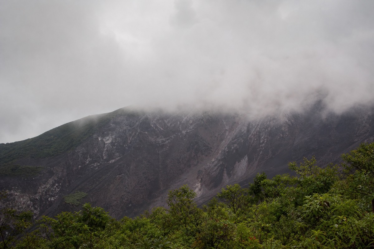 Low green-season cloud rolling across the upper slopes of a volcano in El Salvador with lush vegetation in the foreground and grey sky above