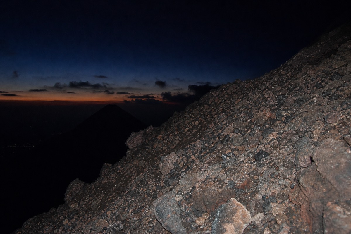 Headlamp beam lighting loose volcanic rock on the upper Santa Ana trail before dawn