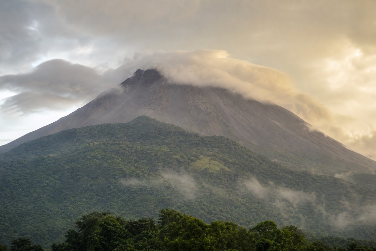 Low cloud pouring over the crater rim of Santa Ana Volcano in soft morning light with green slopes below