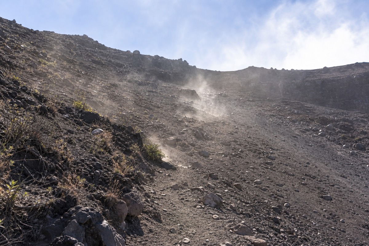 Steep loose rubble on the exposed upper third of the Santa Ana Volcano trail under a bright sky with the rim above