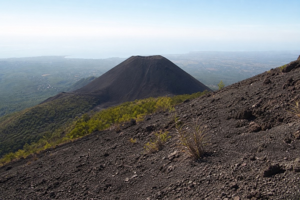 The bare black cone of Izalco volcano seen from a bend on the Santa Ana trail with hazy lowlands stretching behind it