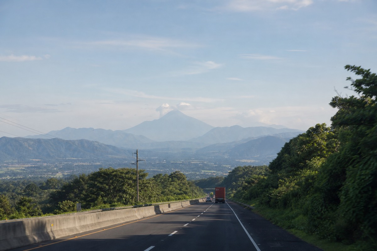 Early morning highway leaving San Salvador toward the western highlands with soft haze over green hills and a volcano outline on the horizon