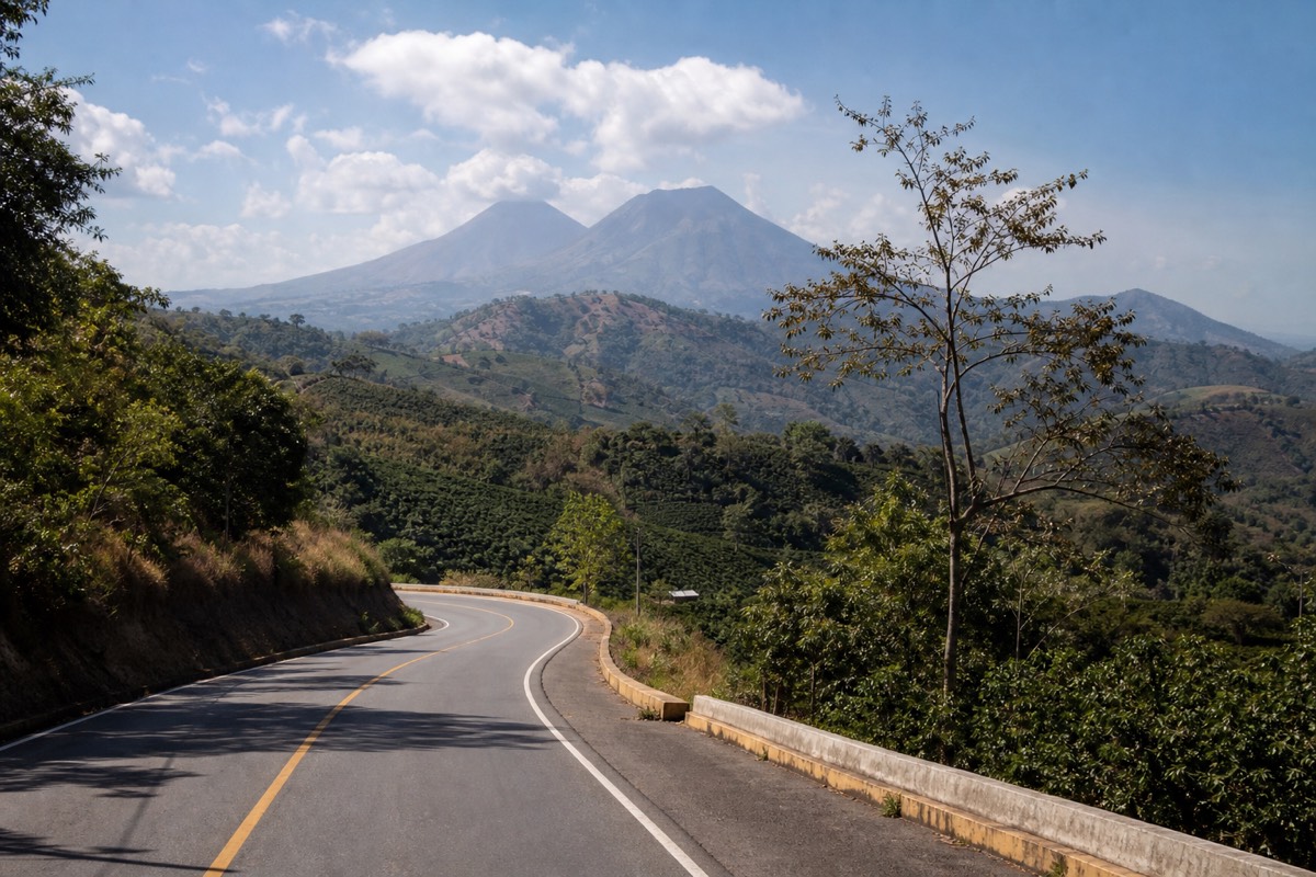 Two-lane highland road in western El Salvador with volcanic peaks rising beyond coffee farms