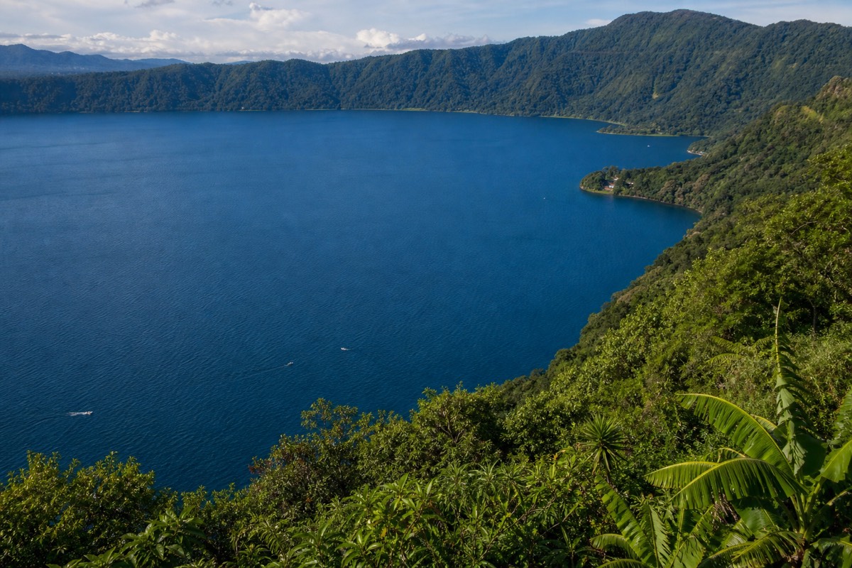 Wide view of the deep blue caldera of Lake Coatepeque with green rim walls under afternoon light