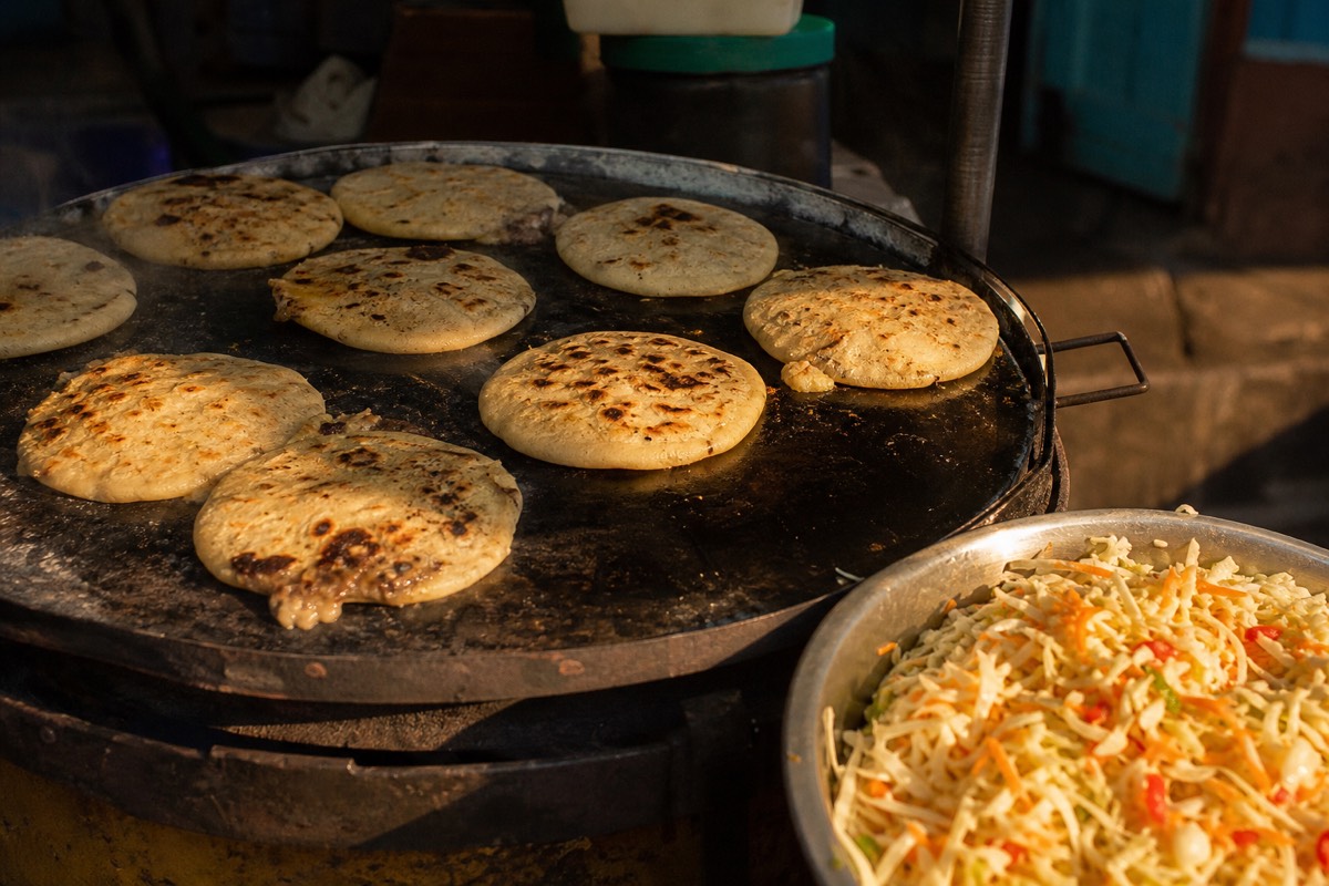 Pupusas cooking on a hot comal griddle at a roadside stand in El Salvador