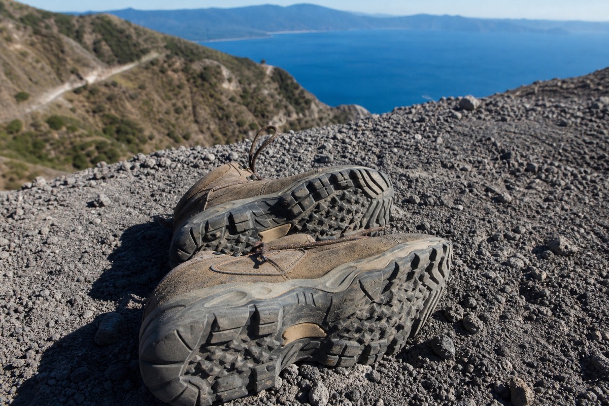 Worn hiking boots with lugged soles resting on loose grey volcanic rock at the edge of the Santa Ana volcano trail
