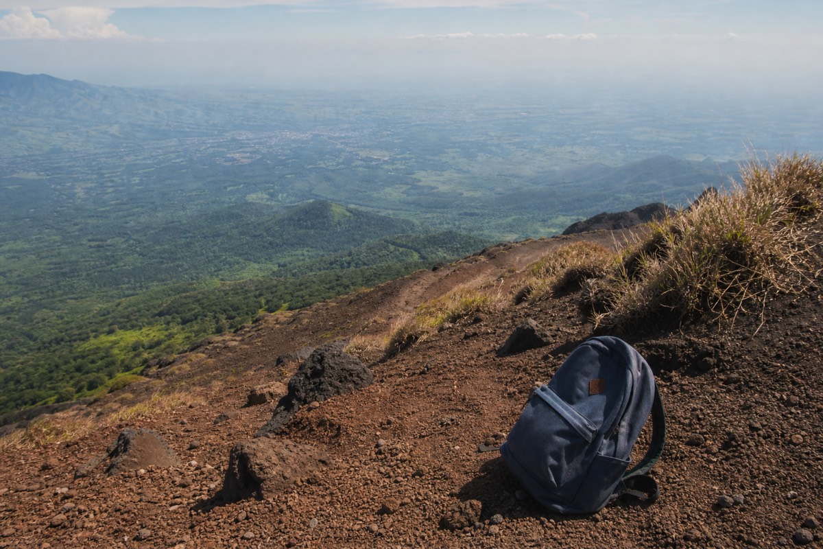 Small daypack resting on the ground beside the open upper trail of Santa Ana volcano with hazy green lowlands behind