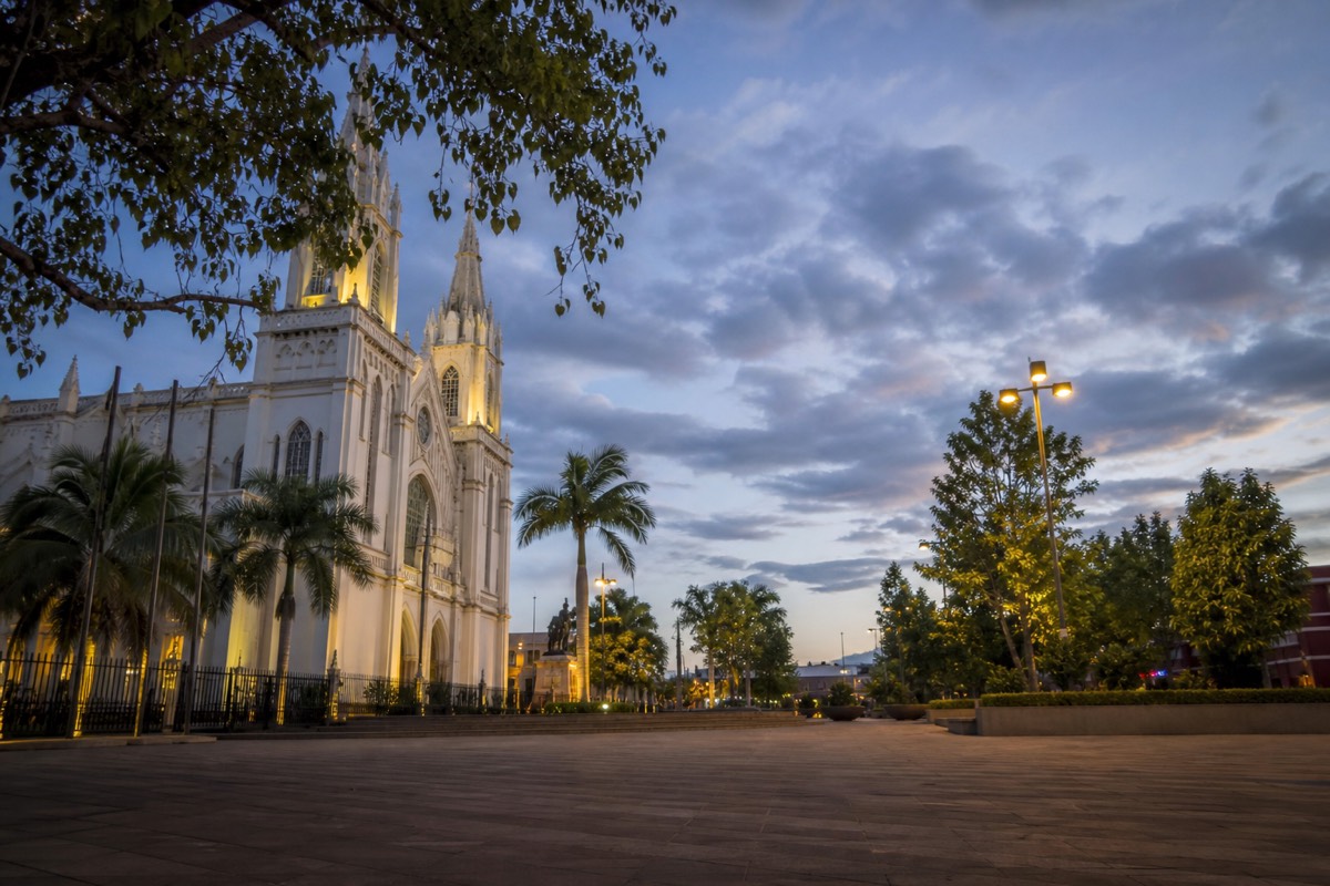 Santa Ana's central plaza at dusk with the cathedral facade lit and people crossing the square