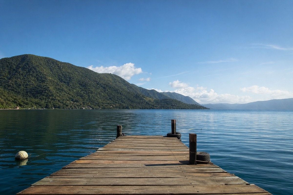 Wooden dock stretching into the calm blue water of Lake Coatepeque with the caldera wall behind